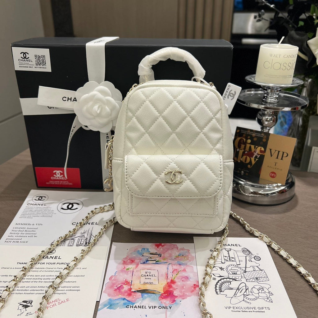 White quilted handbag with chain strap on a table with Chanel branding and VIP materials.